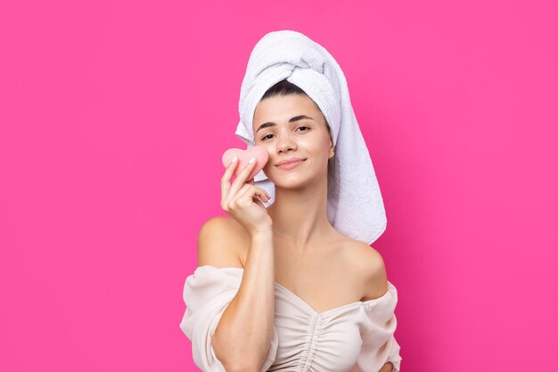 Beautiful cheerful attractive girl with a towel on her head holds a sponge in the form of a pink heart