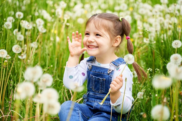A beautiful cheerful funny girl with two tails sits on a field with dandelions and laughs