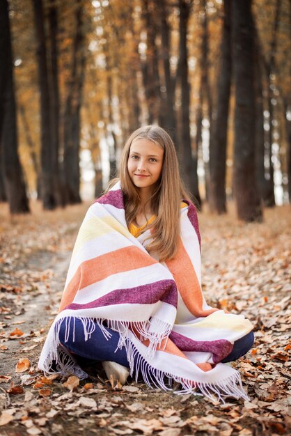 Beautiful cheerful girl sitting on yellow foliage in the park smiling to the camera