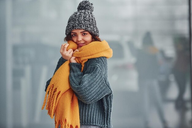 Photo beautiful cheerful girl in yellow scarf and in warm clothes standing indoors against background with reflections.