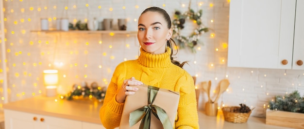 Beautiful cheerful happy young girl with christmas gifts on the background of the new year kitchen