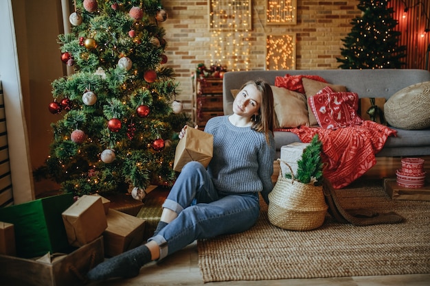 Bella ragazza allegra felice con i regali di natale sul pavimento vicino all'albero di capodanno a casa