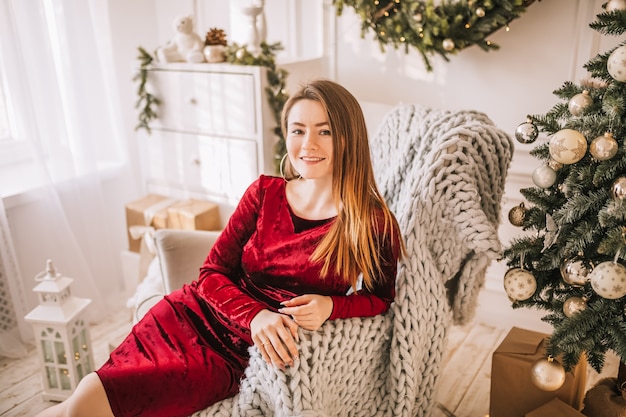 Beautiful cheerful happy young girl with christmas gifts on sofa on the background of a new year tree at home