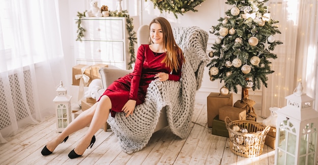 Beautiful cheerful happy young girl with christmas gifts on sofa on the background of a new year tree at home