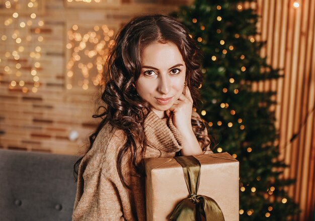 Beautiful cheerful happy young girl with christmas gifts on sofa on the of a new year tree at home