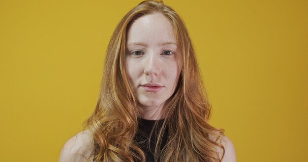 Beautiful cheerful redhead girl smiling laughing looking at camera over yellow background.