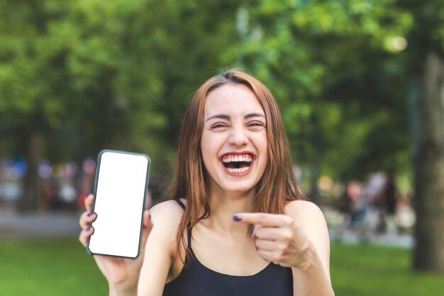 空のスマートフォンで笑って、デザインと広告の目的でその画面を指している美しい陽気なトルコの女性