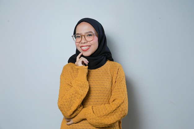 オレンジ色のセーターと眼鏡を身に着けている美しい陽気な若いアジアのイスラム教徒のビジネス女性