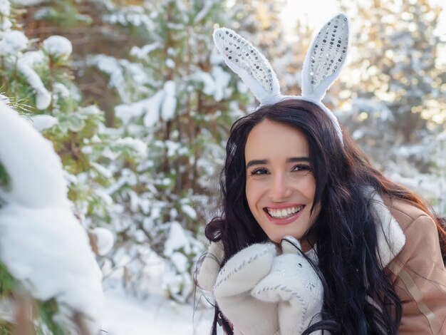 Beautiful cheerful young woman with bunny ears on her head in winter fairy forest, the concept of Christmas and new year holidays