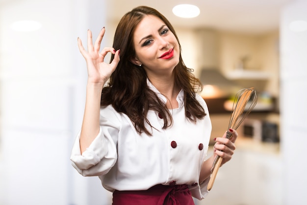 Beautiful chef woman making OK sign on unfocused background