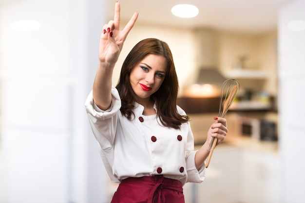 Beautiful chef woman making victory gesture on unfocused background