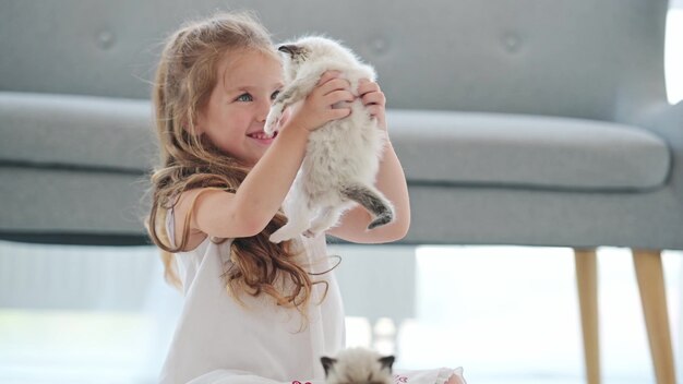 Красивая детская девочка, держа в руках пушистого котенка тряпичной куклы, глядя на него и улыбаясь. Счастливый ребенок с маленьким котенком