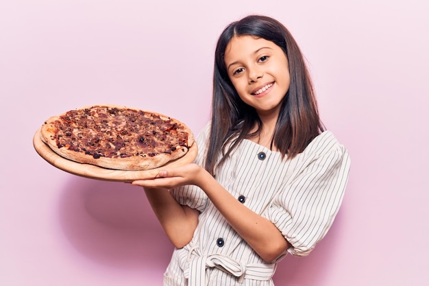 Photo beautiful child girl holding italian pizza looking positive and happy standing and smiling with a confident smile showing teeth