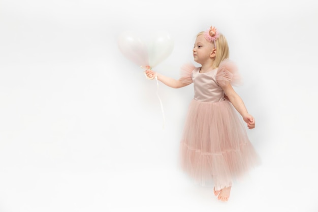 Beautiful child in lush pink dress with tulle skirt holds balloons in hands Little elegant girl isolated on white background