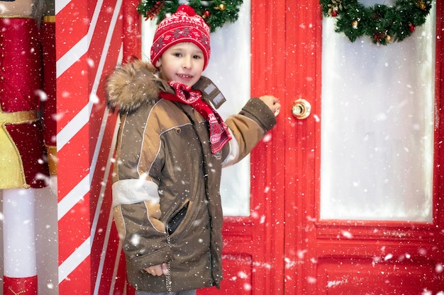 A beautiful child in winter clothes is standing near the red doors