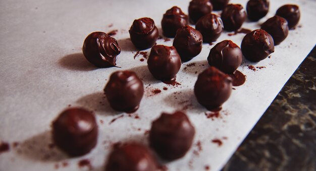 Bellissimi tartufi di cioccolato immersi nella massa di cioccolato fuso e scintillanti con cacao in polvere su carta bianca da forno su un tavolo di marmo. avvicinamento