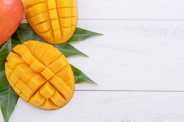 Photo beautiful chopped ripe mango with green leaves on bright white color wooden background top view flat lay copy space tropical fruit design concept