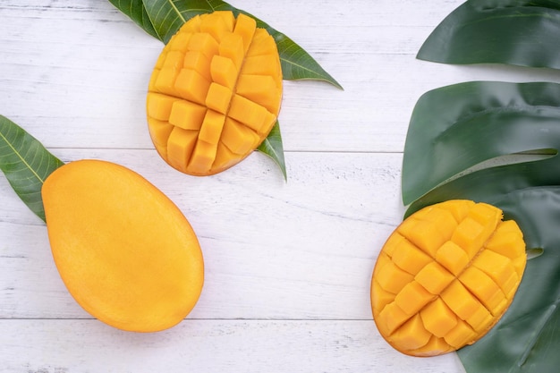 Beautiful chopped ripe mango with green leaves on bright white color wooden background top view flat lay copy space Tropical fruit design concept