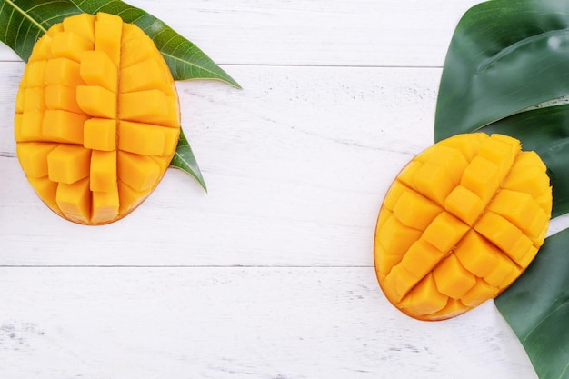 Beautiful chopped ripe mango with green leaves on bright white color wooden background top view flat lay copy space Tropical fruit design concept