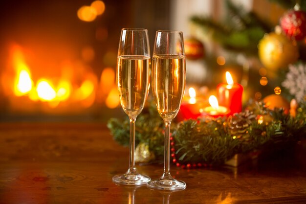 Beautiful Christmas background with two champagne flutes, burning fireplace and wreath with candles