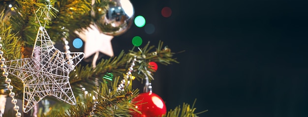 Beautiful Christmas decor concept, bauble hanging on the Christmas tree with sparkling light spot, blurry dark black background, macro detail, close up.