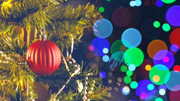 Beautiful Christmas decor concept, bauble hanging on the Christmas tree with sparkling light spot, blurry dark black background, macro detail, close up.