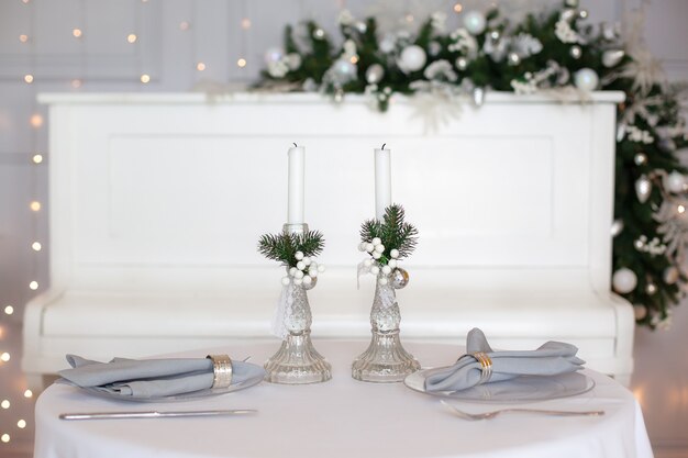 美しいクリスマスディナーの設定。冬の装飾と白いキャンドルの中でテーブルクロスでお祝いテーブルの設定。トップビュー、フラットレイアウト。クリスマスや感謝祭の家族の夕食の概念。