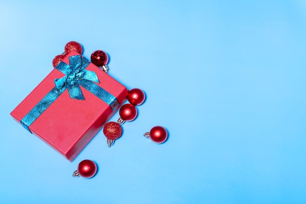 Beautiful Christmas red balls and a red gift with a green ribbon decorating toys on a blue background Flat lay festive mockup with copy space