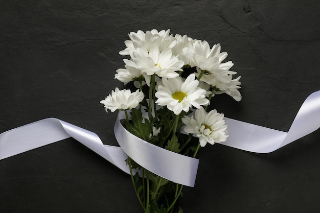 Photo beautiful chrysanthemum flowers and white ribbon on black table top view funeral symbols