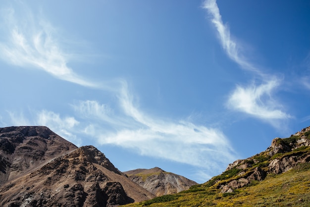 Beautiful cirrus clouds in blue sky over rocks in sunlight.