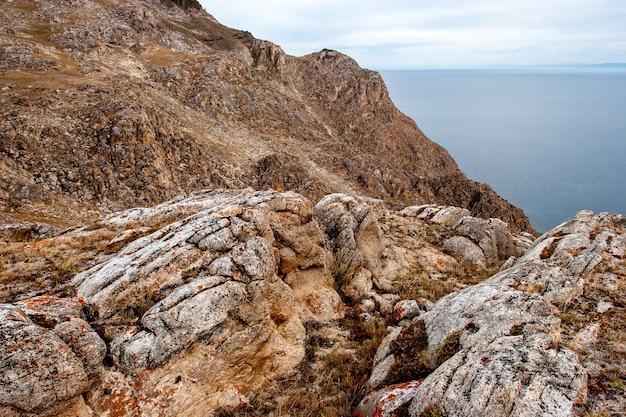 Beautiful cliffs by the lake. The stones are ancient and cracked. A lake without waves. The sky with clouds.