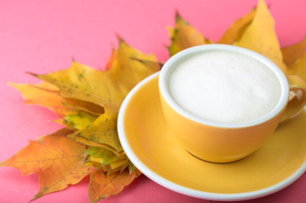 Beautiful coffee yellow cup with  cappuccino on pink background and maple leaves near