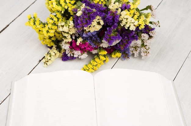 Beautiful colorful flowers and open blank book on a white wooden table