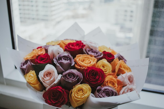 beautiful colorful natural roses arrangement bouquet with wrapping paper in front of the window