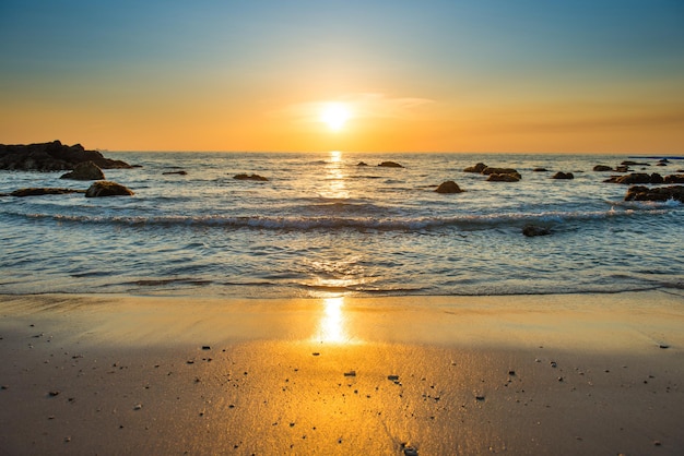 Beautiful colorful sunset landscape with sand beach, golden sun and stones at sea shore