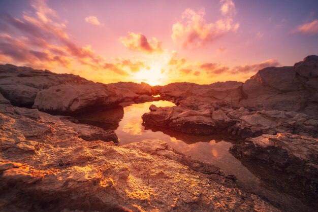 Beautiful colorful sunset near the sea at Cyprus with dramatic clouds and boulders. Reflections in the water. Beauty world natural outdoors travel background