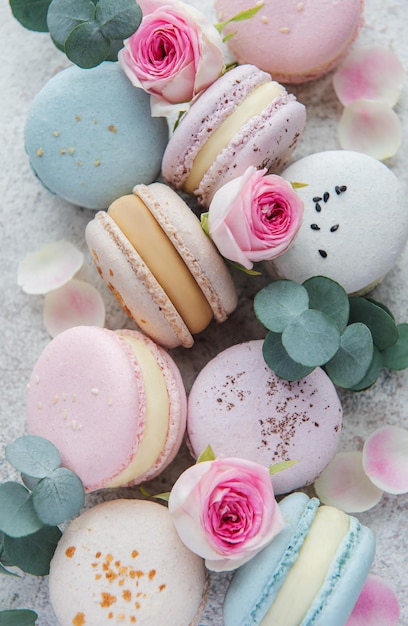 Bellissimi amaretti colorati e gustosi e rose rosa su uno sfondo di cemento grigio