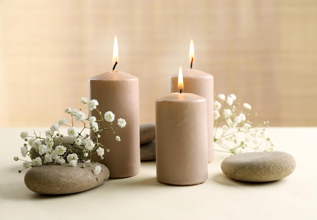 Beautiful composition of alight candles with pebbles and flowers on the table