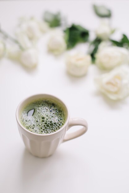 Красивая композиция с чашкой зеленого чая маття и розами на белом фоне