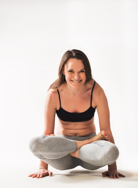 Foto bella concentrato giovane atleta donna caucasica facendo complesso yoga avanzato asana in piedi sul pavimento su sfondo bianco