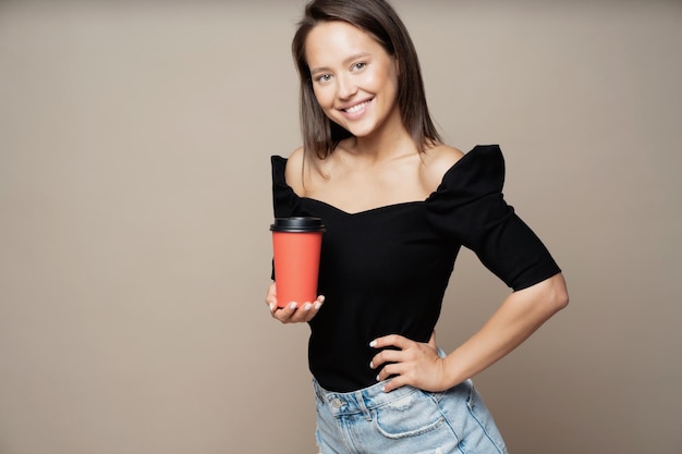 Beautiful confident young woman brunette posing looking at the camera He holds a paper Cup