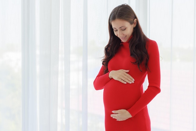 Foto una bella donna incinta si fermò con le mani sul ventre e toccò il nascituro teneramente e felicemente con una faccia sorridente