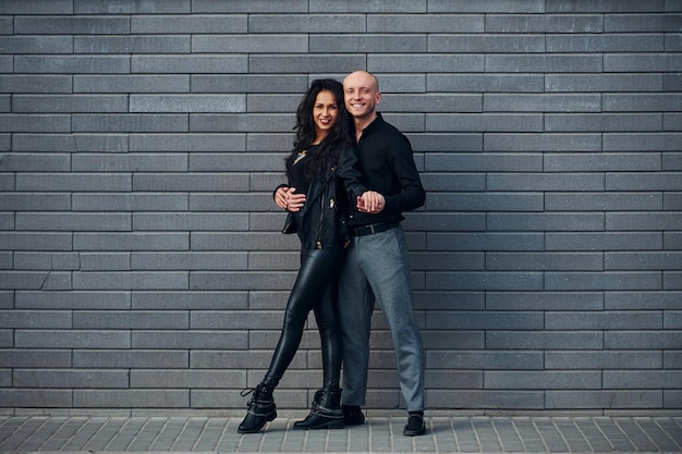 Beautiful couple in black clothes dancing together against wall outdoors