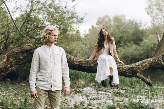 A beautiful couple in the boo style embraces sitting on a branch over the lake