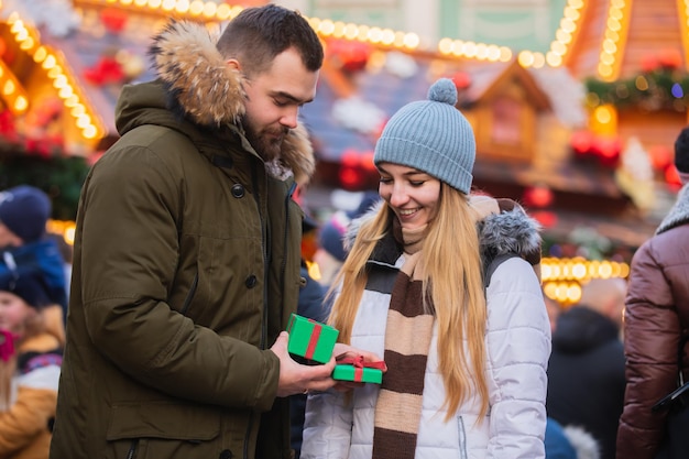 美しいカップル、ボーイフレンドは、ポーランドのヴロツワフでのクリスマスフェアでガールフレンドにプレゼントギフトボックスを与えます