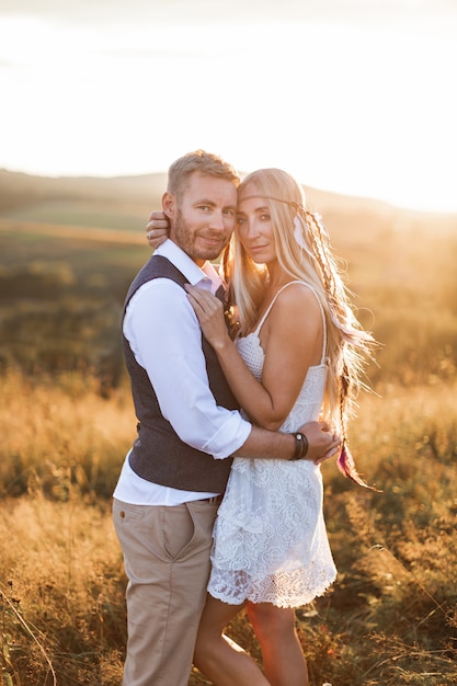 Beautiful couple dressed in boho style embracing each other in the sunny summer field