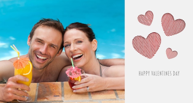 Beautiful couple drinking cocktails in the swimming pool against cute valentines message