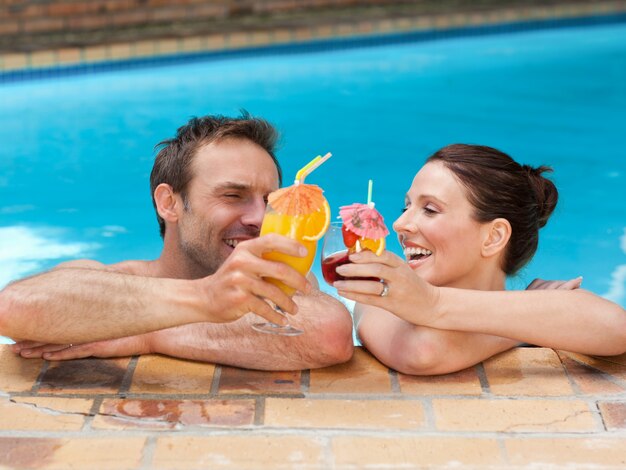 Beautiful couple drinking cocktails in the swimming pool