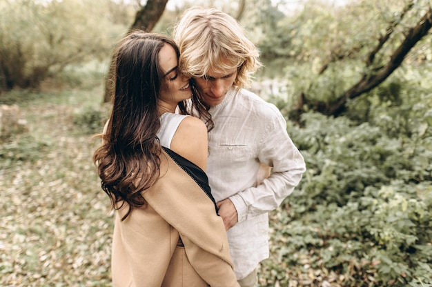 A beautiful couple in free clothes walks in the lawn near the lake on a sunny summer day