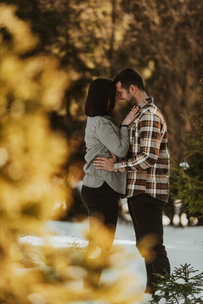 Beautiful couple hugging between snowy pines woman in casual clothes holding hands on man chest Selective focus